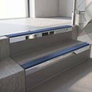 Square-edge aluminium stair nosing with a deep 56mm riser face in Bright Polished, fitted along two vinyl-covered concrete steps in an office stairwell, with a Blue anti-slip PVC insert running the full width of each step