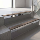 Square-edge aluminium stair nosing with a deep 56mm riser face in Bright Polished, fitted along two vinyl-covered concrete steps in an office stairwell, with a Brown anti-slip PVC insert running the full width of each step