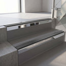 Square-edge aluminium stair nosing with a deep 56mm riser face in Bright Polished, fitted along two vinyl-covered concrete steps in an office stairwell, with a Dark Grey anti-slip PVC insert running the full width of each step
