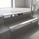Square-edge aluminium stair nosing with a deep 56mm riser face in Bright Polished, fitted along two vinyl-covered concrete steps in an office stairwell, with an Oyster anti-slip PVC insert running the full width of each step