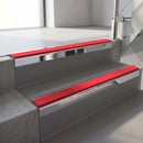 Square-edge aluminium stair nosing with a deep 56mm riser face in Bright Polished, fitted along two vinyl-covered concrete steps in an office stairwell, with a Red anti-slip PVC insert running the full width of each step
