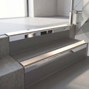Square-edge aluminium stair nosing with a deep 56mm riser face in Bright Polished, fitted along two vinyl-covered concrete steps in an office stairwell, with a Sahara anti-slip PVC insert running the full width of each step