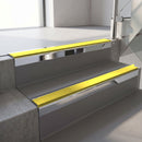 Square-edge aluminium stair nosing with a deep 56mm riser face in Bright Polished, fitted along two vinyl-covered concrete steps in an office stairwell, with a Yellow anti-slip PVC insert running the full width of each step