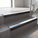 Square-edge aluminium stair nosing with a deep 56mm riser face in Dark Bronze, fitted along two vinyl-covered concrete steps in an office stairwell, with an Aura anti-slip PVC insert running the full width of each step