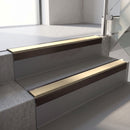 Square-edge aluminium stair nosing with a deep 56mm riser face in Dark Bronze, fitted along two vinyl-covered concrete steps in an office stairwell, with a Beige anti-slip PVC insert running the full width of each step