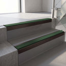 Square-edge aluminium stair nosing with a deep 56mm riser face in Dark Bronze, fitted along two vinyl-covered concrete steps in an office stairwell, with a Dark Green anti-slip PVC insert running the full width of each step