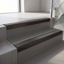 Square-edge aluminium stair nosing with a deep 56mm riser face in Dark Bronze, fitted along two vinyl-covered concrete steps in an office stairwell, with a Dark Grey anti-slip PVC insert running the full width of each step