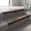 Square-edge aluminium stair nosing with a deep 56mm riser face in Dark Bronze, fitted along two vinyl-covered concrete steps in an office stairwell, with a Mid Brown anti-slip PVC insert running the full width of each step