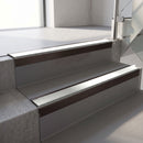 Square-edge aluminium stair nosing with a deep 56mm riser face in Dark Bronze, fitted along two vinyl-covered concrete steps in an office stairwell, with an Oyster anti-slip PVC insert running the full width of each step