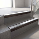 Square-edge aluminium stair nosing with a deep 56mm riser face in Dark Bronze, fitted along two vinyl-covered concrete steps in an office stairwell, with a Polar Grey anti-slip PVC insert running the full width of each step