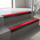 Square-edge aluminium stair nosing with a deep 56mm riser face in Dark Bronze, fitted along two vinyl-covered concrete steps in an office stairwell, with a Red anti-slip PVC insert running the full width of each step