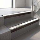 Square-edge aluminium stair nosing with a deep 56mm riser face in Dark Bronze, fitted along two vinyl-covered concrete steps in an office stairwell, with a White anti-slip PVC insert running the full width of each step