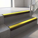 Square-edge aluminium stair nosing with a deep 56mm riser face in Dark Bronze, fitted along two vinyl-covered concrete steps in an office stairwell, with a Yellow anti-slip PVC insert running the full width of each step