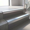 Square-edge aluminium stair nosing with a deep 56mm riser face in Mill Finish, fitted along two vinyl-covered concrete steps in an office stairwell, with an Aura anti-slip PVC insert running the full width of each step