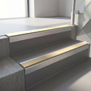 Square-edge aluminium stair nosing with a deep 56mm riser face in Mill Finish, fitted along two vinyl-covered concrete steps in an office stairwell, with a Beige anti-slip PVC insert running the full width of each step