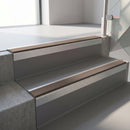 Square-edge aluminium stair nosing with a deep 56mm riser face in Mill Finish, fitted along two vinyl-covered concrete steps in an office stairwell, with a Brown anti-slip PVC insert running the full width of each step