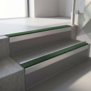 Square-edge aluminium stair nosing with a deep 56mm riser face in Mill Finish, fitted along two vinyl-covered concrete steps in an office stairwell, with a Dark Green anti-slip PVC insert running the full width of each step