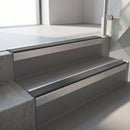 Square-edge aluminium stair nosing with a deep 56mm riser face in Mill Finish, fitted along two vinyl-covered concrete steps in an office stairwell, with a Dark Grey anti-slip PVC insert running the full width of each step