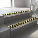 Square-edge aluminium stair nosing with a deep 56mm riser face in Mill Finish, fitted along two vinyl-covered concrete steps in an office stairwell, with a Hazard anti-slip PVC insert running the full width of each step