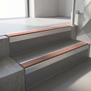 Square-edge aluminium stair nosing with a deep 56mm riser face in Mill Finish, fitted along two vinyl-covered concrete steps in an office stairwell, with a Mid Brown anti-slip PVC insert running the full width of each step