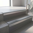 Square-edge aluminium stair nosing with a deep 56mm riser face in Mill Finish, fitted along two vinyl-covered concrete steps in an office stairwell, with a Mid Grey anti-slip PVC insert running the full width of each step