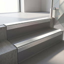 Square-edge aluminium stair nosing with a deep 56mm riser face in Mill Finish, fitted along two vinyl-covered concrete steps in an office stairwell, with an Oyster anti-slip PVC insert running the full width of each step