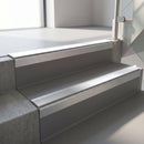 Square-edge aluminium stair nosing with a deep 56mm riser face in Mill Finish, fitted along two vinyl-covered concrete steps in an office stairwell, with a Polar Grey anti-slip PVC insert running the full width of each step