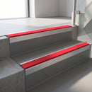 Square-edge aluminium stair nosing with a deep 56mm riser face in Mill Finish, fitted along two vinyl-covered concrete steps in an office stairwell, with a Red anti-slip PVC insert running the full width of each step