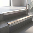 Square-edge aluminium stair nosing with a deep 56mm riser face in Mill Finish, fitted along two vinyl-covered concrete steps in an office stairwell, with a Sahara anti-slip PVC insert running the full width of each step