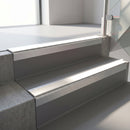 Square-edge aluminium stair nosing with a deep 56mm riser face in Mill Finish, fitted along two vinyl-covered concrete steps in an office stairwell, with a White anti-slip PVC insert running the full width of each step