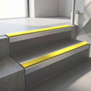 Square-edge aluminium stair nosing with a deep 56mm riser face in Mill Finish, fitted along two vinyl-covered concrete steps in an office stairwell, with a Yellow anti-slip PVC insert running the full width of each step