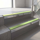 Square-edge aluminium stair nosing with a deep 56mm riser face in Mirroflect Silver, fitted along two vinyl-covered concrete steps in an office stairwell, with an Apple Green anti-slip PVC insert running the full width of each step