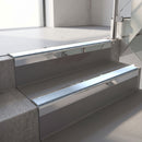 Square-edge aluminium stair nosing with a deep 56mm riser face in Mirroflect Silver, fitted along two vinyl-covered concrete steps in an office stairwell, with an Aura anti-slip PVC insert running the full width of each step