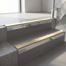 Square-edge aluminium stair nosing with a deep 56mm riser face in Mirroflect Silver, fitted along two vinyl-covered concrete steps in an office stairwell, with a Beige anti-slip PVC insert running the full width of each step