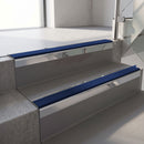Square-edge aluminium stair nosing with a deep 56mm riser face in Mirroflect Silver, fitted along two vinyl-covered concrete steps in an office stairwell, with a Dark Blue anti-slip PVC insert running the full width of each step