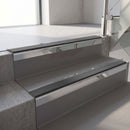 Square-edge aluminium stair nosing with a deep 56mm riser face in Mirroflect Silver, fitted along two vinyl-covered concrete steps in an office stairwell, with a Dark Grey anti-slip PVC insert running the full width of each step