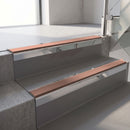 Square-edge aluminium stair nosing with a deep 56mm riser face in Mirroflect Silver, fitted along two vinyl-covered concrete steps in an office stairwell, with a Mid Brown anti-slip PVC insert running the full width of each step