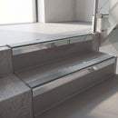 Square-edge aluminium stair nosing with a deep 56mm riser face in Mirroflect Silver, fitted along two vinyl-covered concrete steps in an office stairwell, with a Mid Grey anti-slip PVC insert running the full width of each step