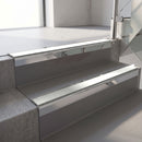 Square-edge aluminium stair nosing with a deep 56mm riser face in Mirroflect Silver, fitted along two vinyl-covered concrete steps in an office stairwell, with an Oyster anti-slip PVC insert running the full width of each step
