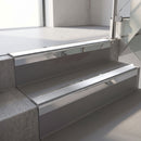 Square-edge aluminium stair nosing with a deep 56mm riser face in Mirroflect Silver, fitted along two vinyl-covered concrete steps in an office stairwell, with a Polar Grey anti-slip PVC insert running the full width of each step