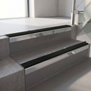 Square-edge aluminium stair nosing with a deep 56mm riser face in Mirroflect Silver, fitted along two vinyl-covered concrete steps in an office stairwell, with a Premium Black anti-slip PVC insert running the full width of each step