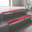 Square-edge aluminium stair nosing with a deep 56mm riser face in Mirroflect Silver, fitted along two vinyl-covered concrete steps in an office stairwell, with a Red anti-slip PVC insert running the full width of each step