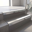 Square-edge aluminium stair nosing with a deep 56mm riser face in Mirroflect Silver, fitted along two vinyl-covered concrete steps in an office stairwell, with a White anti-slip PVC insert running the full width of each step
