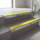 Square-edge aluminium stair nosing with a deep 56mm riser face in Mirroflect Silver, fitted along two vinyl-covered concrete steps in an office stairwell, with a Yellow anti-slip PVC insert running the full width of each step