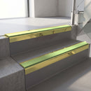 Square-edge aluminium stair nosing with a deep 56mm riser face in Mirrorflect Gold, fitted along two vinyl-covered concrete steps in an office stairwell, with an Apple Green anti-slip PVC insert running the full width of each step