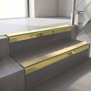 Square-edge aluminium stair nosing with a deep 56mm riser face in Mirrorflect Gold, fitted along two vinyl-covered concrete steps in an office stairwell, with a Beige anti-slip PVC insert running the full width of each step
