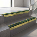 Square-edge aluminium stair nosing with a deep 56mm riser face in Mirrorflect Gold, fitted along two vinyl-covered concrete steps in an office stairwell, with a Dark Green anti-slip PVC insert running the full width of each step