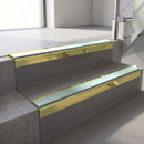 Square-edge aluminium stair nosing with a deep 56mm riser face in Mirrorflect Gold, fitted along two vinyl-covered concrete steps in an office stairwell, with a Sage Green anti-slip PVC insert running the full width of each step