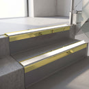 Square-edge aluminium stair nosing with a deep 56mm riser face in Mirrorflect Gold, fitted along two vinyl-covered concrete steps in an office stairwell, with a White anti-slip PVC insert running the full width of each step