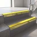 Square-edge aluminium stair nosing with a deep 56mm riser face in Mirrorflect Gold, fitted along two vinyl-covered concrete steps in an office stairwell, with a Yellow anti-slip PVC insert running the full width of each step